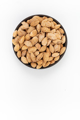 Roasted salty almonds nuts in shells  in round bowl on white background, top view