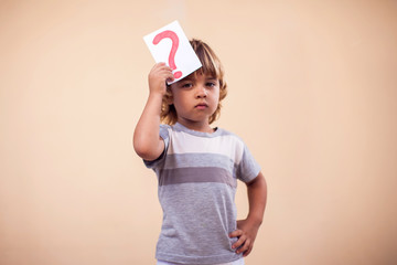 A portrait of kid boy holding cards with question mark. Childhood and education concept