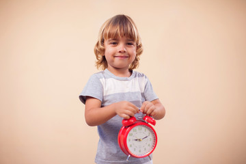 A portrait of kid boy holding alarm clock. Childhood and time management concept