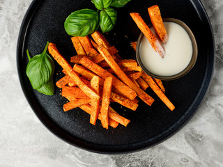 Homemade diet snack - fried carrot sticks with white sauce on table background.