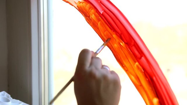 Close up child's hand graws a rainbow on the window during Covid-19 quarantine at home. Chase the rainbow flashmob and staying at home concept.