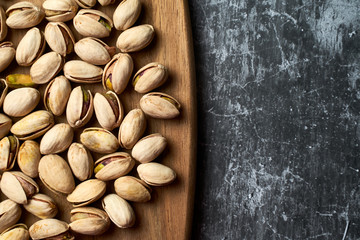 Top view of pistachios on a wooden board on a dark background.