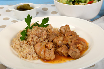 beef stew with onions and barleypieces of fried meat with onions and millet on a white plate next to lettuce