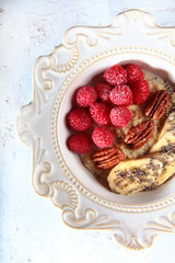 Oatmeal porridge with raspberries, banana and walnuts on a white plate. Macro photo of a dish on a white textured background. Copy of the space.