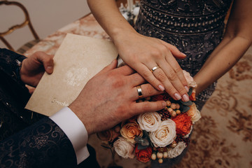 Hands of the bride and groom. Bride and groom holding hands at a wedding ceremony. Wedding rings on the hands of the newlyweds. Hands of the newlyweds on the background of a wedding bouquet