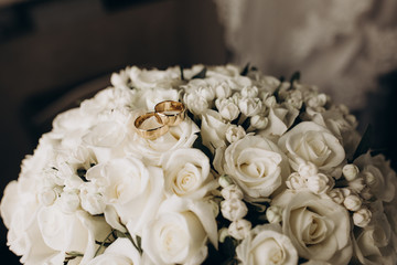 The rings of the newlyweds lie on a beautiful white wedding bouquet. The morning of the bride. Gold rings of the bride and groom on a beautiful background of white roses.