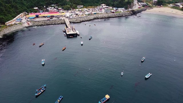 Aerial drone footage of fishermen pier in small fishing village. Fishing boats moored in a bay of Pacific coast in Chile. Los Lagos, Bahia Mansa, Chile