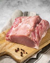 Raw pork carbonade on a wooden plate on the light gray kitchen table. Raw pork meat, tenderloin