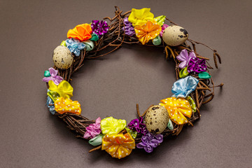 Hand crafted Easter wicker wreath with quail eggs and handmade flowers. Birch branches, polka dot satin ribbon. Stay at home concept. Festive Easter background