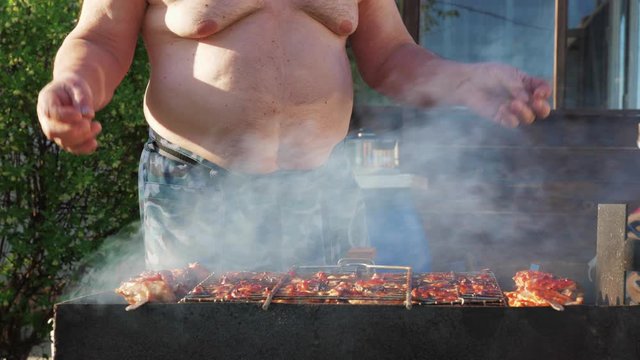 Fat funny man cooks kebabs and dances in the backyard. Unrecognizable man fries meat against the background of nature. The concept of gluttony and an idle lifestyle