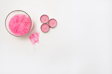 Three light pink candles stand next to the bowl. Nearby, bath salt is poured. Items for spa treatments. Gentle colors. Horizontal photo. Space for text.