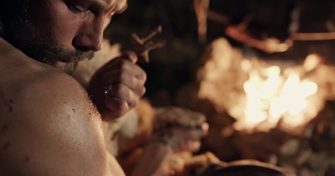 Barbarian taking blood from wound and drawing on stone near fire