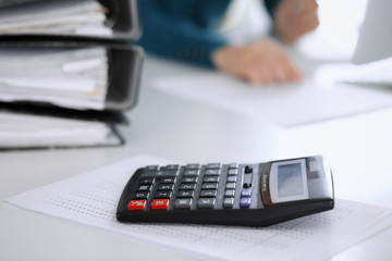 Calculator and binders with papers are waiting to be processed by business woman or bookkeeper working at the desk in office back in blur. Internal Tax and Audit concept