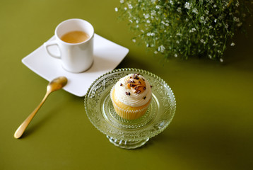 Obraz na płótnie Canvas Vanilla cupcakes with cream cheese frosting and white cup of coffee on green background. Sweet food concept. 