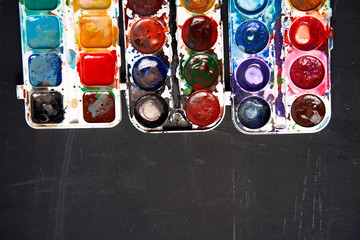 Set of watercolor paints on a black background. Brushes drawing. Creative background. School for teaching drawing.