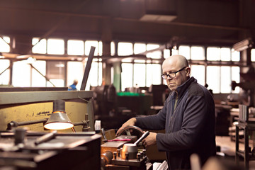 Fototapeta na wymiar A man 50-60 le works at the machine at the factory. Man with glasses. Hard work.
