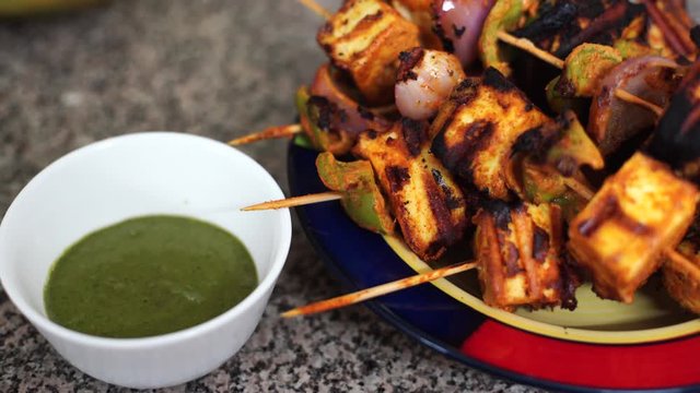 Panning shot of home made grilled tandoori paneer charred with shimla mirch pepper onion tomatoes served with green chutney sauce a popular snack in north India