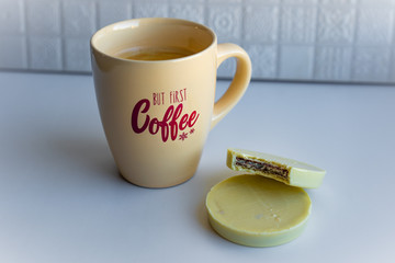 View of a coffee cup with lettering full with black coffee together with round cookies enrobed with white chocolate on white background