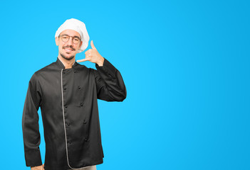 Happy young chef making a gesture of calling with the hand