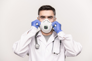 Contemporary clinician in whitecoat, gloves and eyeglasses putting respirator