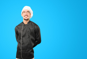 Happy young chef looking against background