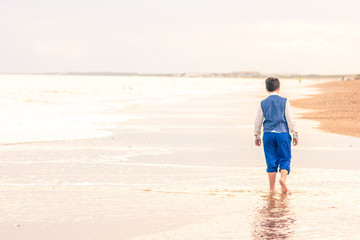 The young Caucasian walks barefoot on the beach near the sea, footprints in the sand