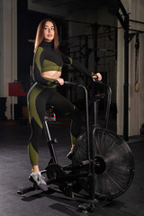 Fototapeta na wymiar Beautiful brunette with elastic buttocks exercises on an air bike. Athletic woman is engaged in the gym on an exercise bike.
