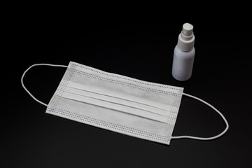 Disposable prevention mask and bottle of disinfectant isolated on black background.