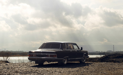Big black russian business car at the bank of Enisey river. Cloudy day. Mafia car dark scene
