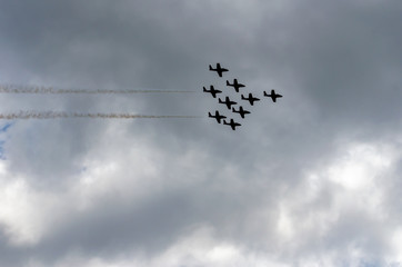 Silhouetted nine jet fighters in formation against gray clouds