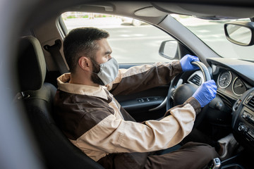 Fototapeta na wymiar Young man in workwear, mask and gloves holding steer while driving to clients
