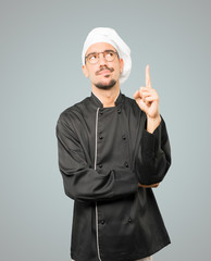 Hesitant young chef pointing up with his finger