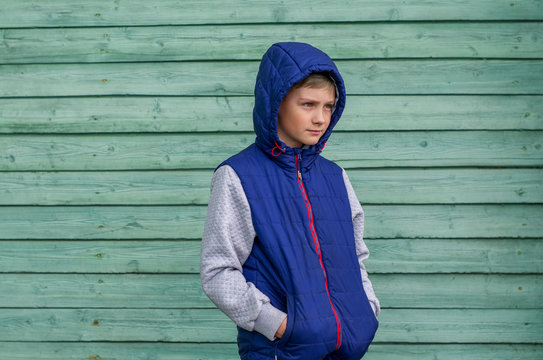 Funny handsome teenage boy is posing for camera. Outdoor portrait of a teenage boy on green background. Expressive boy with a hood on his head
