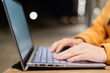 Closeup of female hands on a computer touchpad. Freelancer remotely works on a laptop in the fresh air. A woman is studying on the street in the evening.