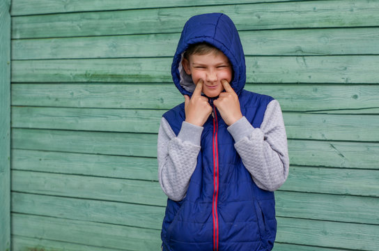 Funny handsome teenage boy is posing for camera. Outdoor portrait of a teenage boy on green background. Expressive boy with a hood on his head