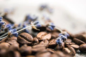 Coffee beans close-up, spilled on the table. Coffee beans on a background of burlap, decorated with branches of dried lavender. Beautifully blurred background. Macro photo.