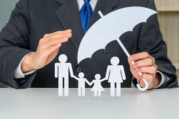 Businessman uses hands and an umbrella to protect family members e.g parents and two child