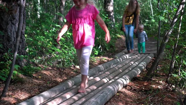 Barefoot family mother with son and daughter walking on tree trunk logs pathway