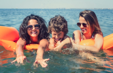 Happy young family positive mom and two little daughters swim on a yellow air mattress in the sea on a sunny summer day during vacation. Vacation concept abroad.