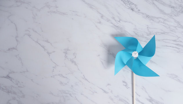 Wind wheel paper real toy on white color marble stone background which made from origami hand made on light blue colour japanese special material and wood stick for baby or kids playing.