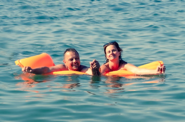 Couple of lovers swim on orange air mattress in the open sea