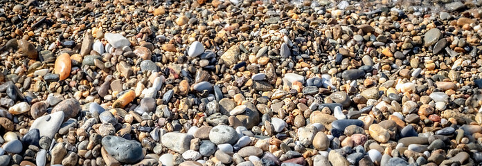 Beautiful summer landscape. Background with small pebbles. Multi-colored sea pebbles covered with clear water. The shore of the beach with sand and pebbles washed by the waves of the sea. Color stones