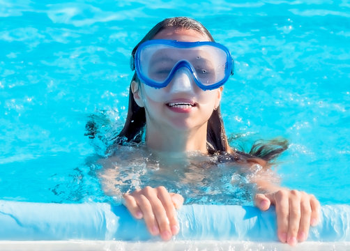 A cute happy young girl child relaxing on the side of a swimming pool wearing golubots goggles.