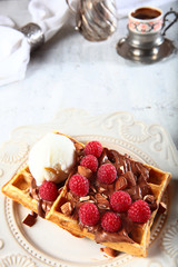 Waffles with chocolate and raspberries. On top of the wafers is a ball of ice cream.Vintage tableware in the background. Dish in a white plate. The concept of morning Breakfast.
