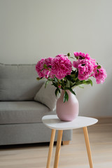 Blooming Pink peony flower with green leaves in pink vase on the white table, in the room, grey background, lifestyle image, copy space © janaland
