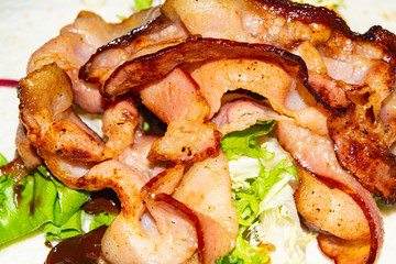 Leafy salad, sliced vegetables, sauce and fried bacon slices on pita bread are the basis for...