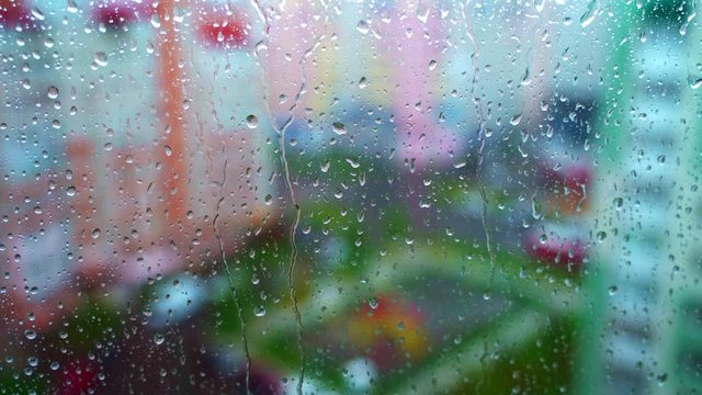 Window at rainy day on blur city background. Wet raindrops on window glass. Abstract raindrop scenery background.
