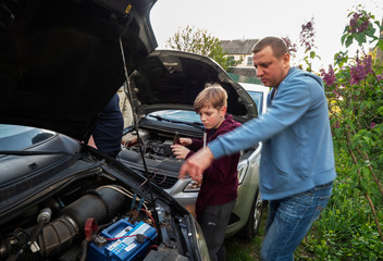 Fototapeta na wymiar The father explains to his son how to properly connect the battery of another car, if necessary, to start his car in case of breakdown of his own battery