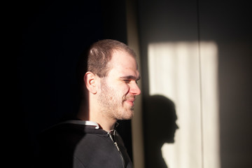 A guy stands in the dark in a blur of sunlight. The young man squints his eyes from the sun. A man...