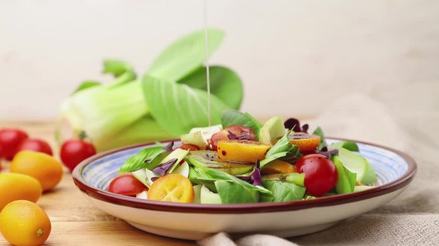 Vegetarian salad of pac choi cabbage, kiwi, tomatoes, kumquat, microgreen sprouts poured with oil. Side view, close up.